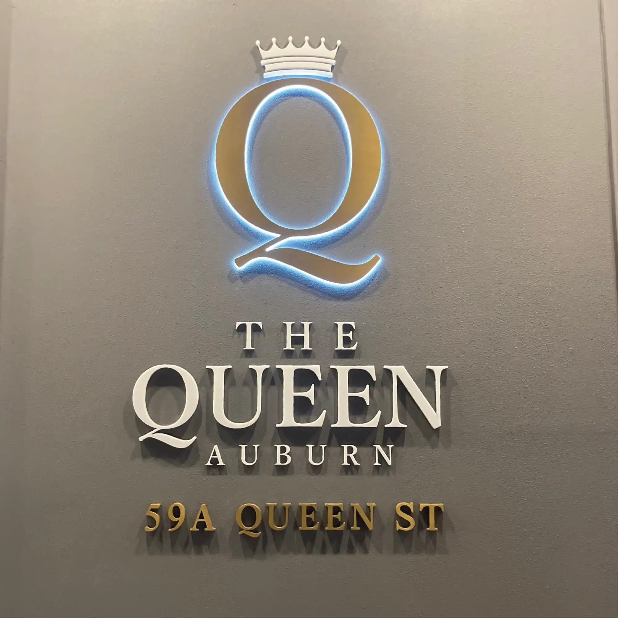 A gold-colored, illuminated ’Q’ logo with a crown, accompanied by white and gold lettering for a business or residence.