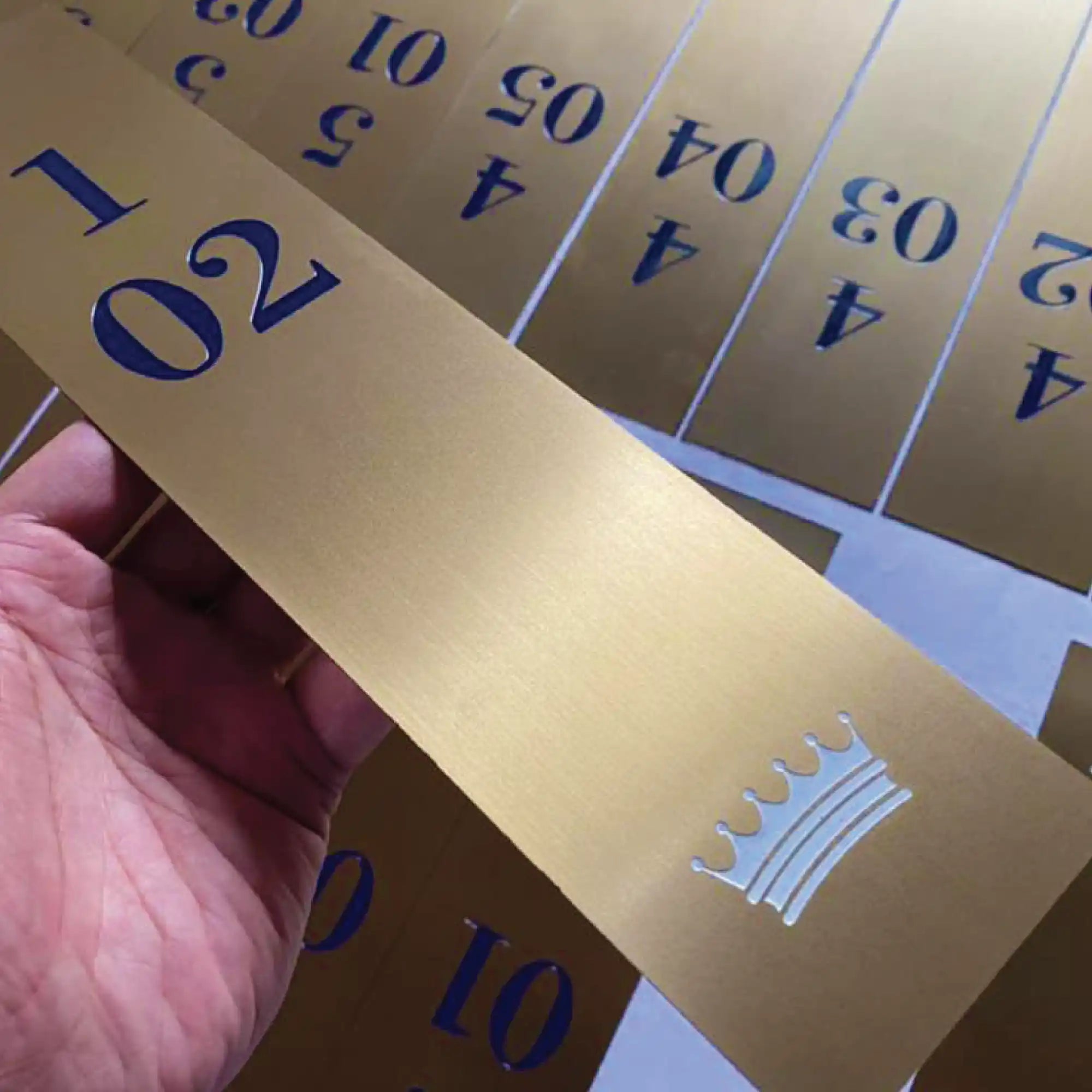 Gold-colored, rectangular strips with blue numbers and a crown emblem.