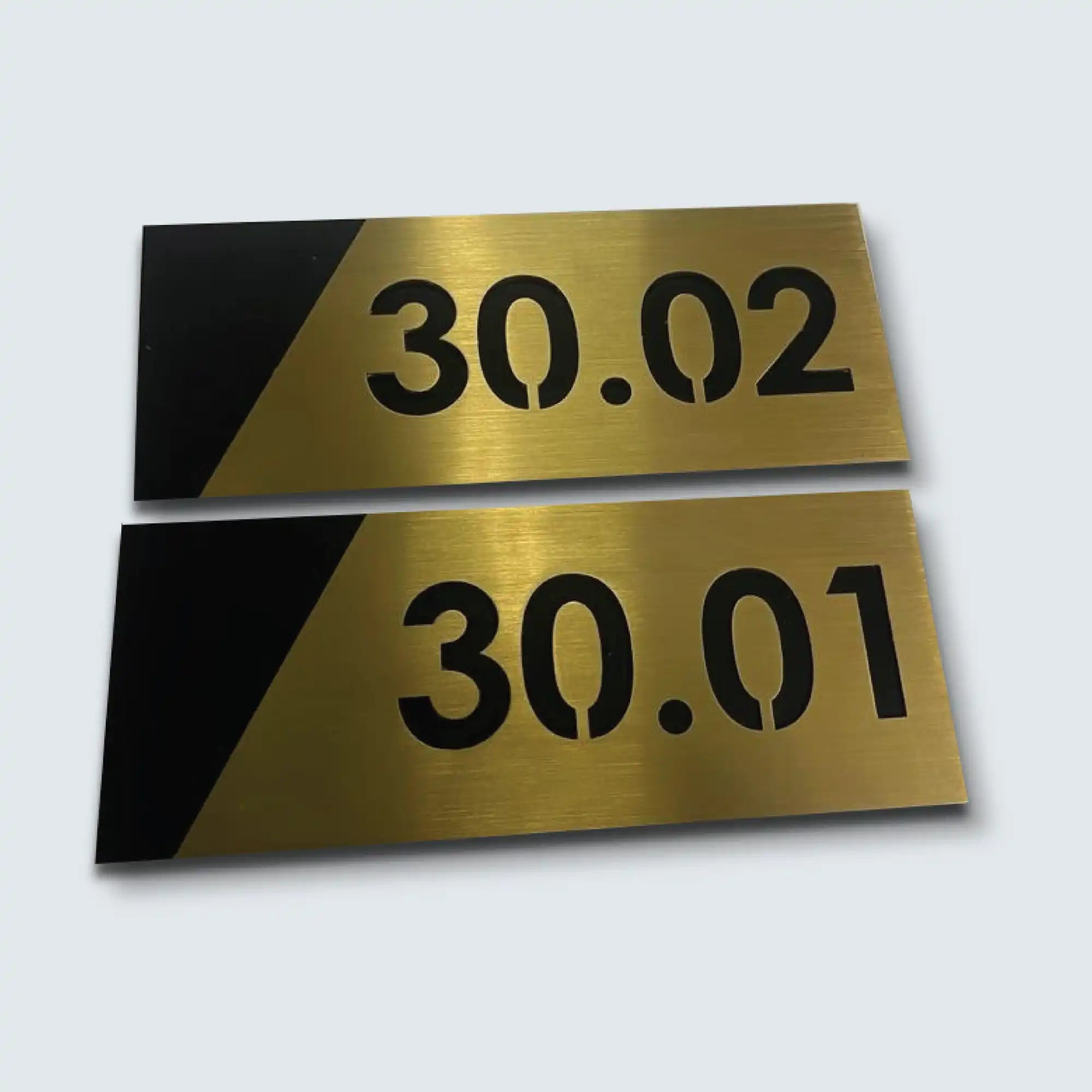 Two rectangular brass-colored signs with black numbers and a black diagonal accent.