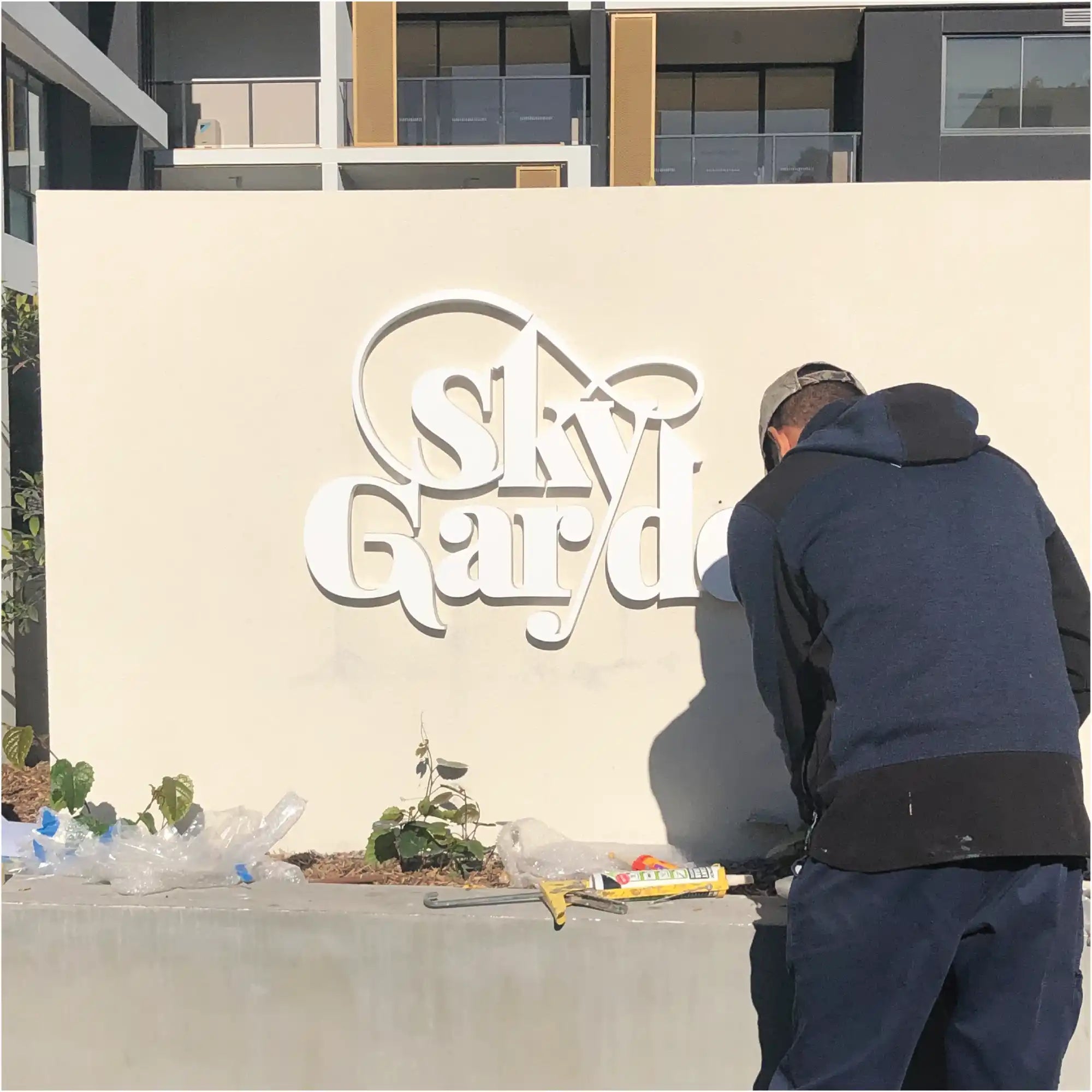 White decorative ’Sky Garden’ signage being installed on a cream-colored wall.